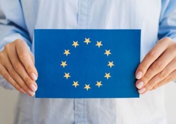 Person holding a blue card displaying the European Union flag: circle of 12 gold stars around a center space.